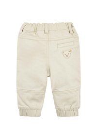 Beige kinderbroek met een elastische tailleband, met een achterzak en een klein geborduurd berenmotief op de voorkant. Zacht, rekbaar materiaal.
