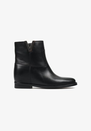Czarne skórzane botki za kostkę z okrągłym noskiem, niskim obcasem i charakterystycznym złotym akcentem w kształcie litery V przy kołnierzu. Gładka tekstura, minimalistyczny design.