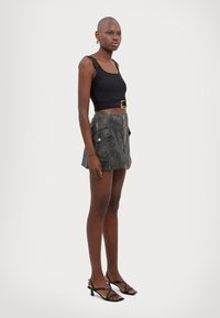 Top nero senza maniche con spalline larghe, abbinato a una mini gonna in pelle grigia a vita alta con tasche laterali e zip frontale. Tacchi neri a strisce.