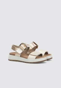 Sandalias bicolor en crema y dorado metálico, con una gran hebilla y correas ajustables, además de una suela texturizada para mayor agarre y comodidad.