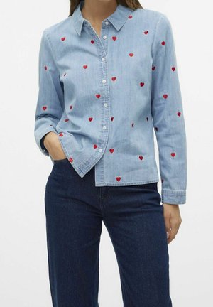 Chemise en denim bleu clair avec des cœurs rouges brodés, devant à boutons et col. Manches longues avec poignets boutonnés. Coupe décontractée.