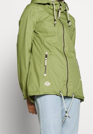 Green hooded jacket with front zipper, two zippered pockets, white drawstrings at hood and hem, worn with light blue jeans.