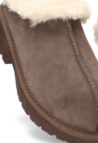 Zapatilla de ante marrón con forro grueso de felpa y suela de goma resistente, diseñada para proporcionar calidez y comodidad en interiores.