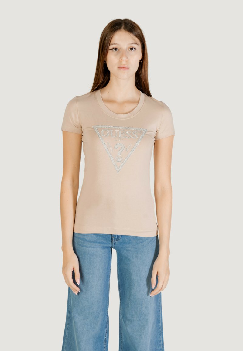 T-shirt aderente beige con scollatura rotonda e maniche corte. Presenta un logo triangolare scintillante con il testo "GUESS?" al centro.