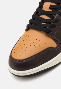 Ādas sporta apavi ar brūnu un brūnganu virsotni, melnām auklām un perforētu purngalu ventilācijai. Iekļauj baltu starppaliku un teksturētu zoli.