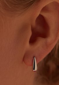 Boucles d'oreilles en argent en forme de goutte, présentant une surface lisse et polie ainsi qu'une forme allongée, mises en valeur en gros plan sur la peau.