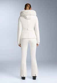 Jachetă albă de ski cu glugă căptușită cu blană, talie ajustată și mâneci lungi, asortată cu pantaloni de ski evazați cu gâte cu fermoar.