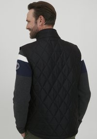 Fekete steppelt mellény magas gallérral, szürke kötött ujjakkal, fehér és sötétkék csíkokkal. A bal karján kör alakú logó található.