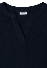 Donkerblauwe gestructureerde blouse met een gespleten V-hals en een wit label met de tekst "CECIL" genaaid aan de binnenkant van de kraag.
