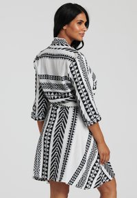 Abito a righe in bianco e nero con colletto, maniche lunghe arrotolate e vita con cinturino. Presenta disegni geometrici e una vestibilità rilassata.