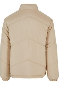 Beige pufferjakke med h�øy krage, med horisontalt quiltet søm og elastiske mansjetter. Glatt stoff med en lett design.