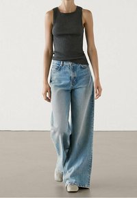 Top grigio senza maniche abbinato a jeans a gamba larga blu chiaro, con un fit rilassato e una texture denim liscia. Accentuato da dettagli di cucitura sottili.