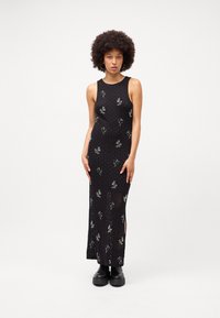 Rochie lungă tricotată neagră cu broderie florală, design fără mâneci, slituri laterale și o siluetă ajustată. Pur și simplu cu cizme negre masive.