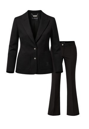 Blazer nero su misura con due bottoni argento a forma di stella e pantaloni neri svasati abbinati con un bottone a stella argento sulla cintura.