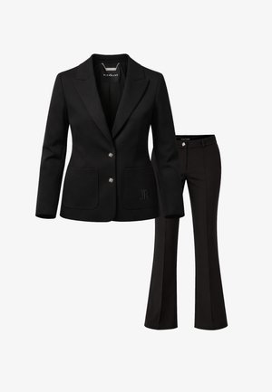 Blazer nero su misura con due bottoni argento a forma di stella e pantaloni neri svasati abbinati con un bottone a stella argento sulla cintura.