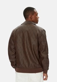 Giubbotto bomber marrone con un delicato motivo su tutta la superficie, materiale elegante, colletto a pressione e polsini e orlo a coste. Sotto, tessuto chiaro e uniforme.