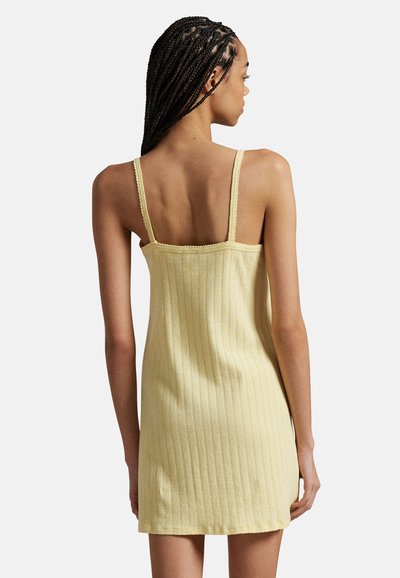 Yellow ribbed dress with thin straps, fitted design, textured fabric, and a straight hem. Simple back view showcasing neckline and strap details.