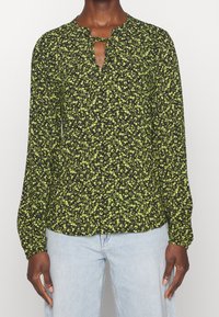 Blouse à manches longues en tissu noir avec un petit motif floral vert, présentant un détail en forme de goutte d'eau au niveau du col et des poignets froncés.