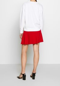 Bílý svetr s kulatým výstřihem, v kombinaci s červenou rozšířenou sukní se svislým žebrováním, doplněný černými lakovanými podpatky.