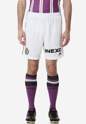 Shorts da calcio bianchi con logo "INEXO" nero ed emblema verde. Abbinati a calze viola con strisce nere, bianche e viola. Scarponi neri.
