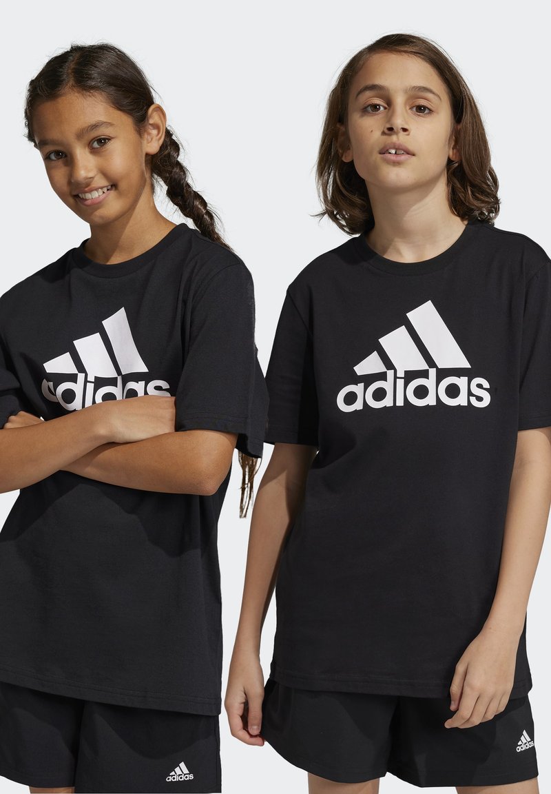 T-shirt in cotone nero con grande logo bianco Adidas sul davanti, abbinato a pantaloni corti sportivi neri con un piccolo logo. Sono presenti due modelli in posa.