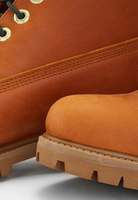 Brązowe skórzane buty o gładkiej teksturze, z okrągłymi mosiężnymi oczkami, grubymi sznurówkami i wytrzymałą gumową podeszwą z głębokim bieżnikiem.