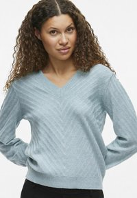 Lyseblå v-hals genser med teksturert herringbone-mønster, lange ermer og ribbestrikkede mansjetter. Glatt strikket stoff med avslappet passform.