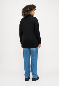 Juodas megztinis su aukštu apykakle ir tekstūruotu peties detailiu, derinamas su šviesiai mėlynomis džinsinėmis kelnėmis ir juodais platforminiais batais.