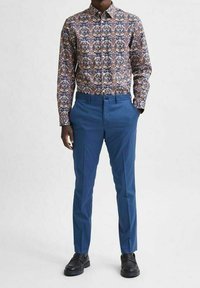 Košile s dlouhým rukávem na knoflíky s barevným květinovým vzorem, doplněná o střihané modré kalhoty a černé nazouvací boty.