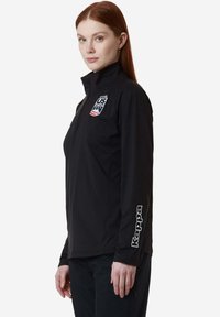 Giacca nera con zip a metà collo con logo del Team Ski USA sul petto e branding "Kappa" sulla manica. Tessuto liscio e leggero.