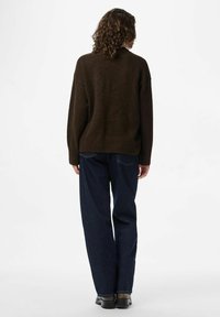 Brown sweater with a ribbed hem, loose fit, and long sleeves, paired with dark blue straight-leg jeans and black shoes.