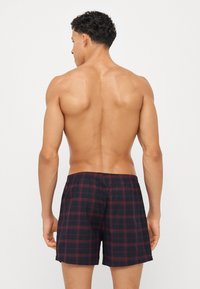 Herre svømmebukser i marineblå med rødt rutemønster. Laget av lett materiale med elastisk midjebånd og en avslappet passform.