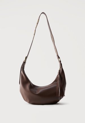 Sac à bandoulière en cuir marron avec des clous dorés sur la sangle et un gland en cuir sur la fermeture éclair, présenté sur un fond uni.