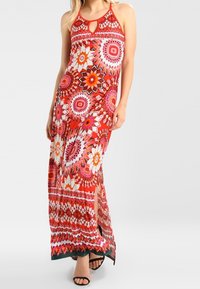Vestido maxi con escote halter, detalle de ojo de cerradura y vibrante patrón floral rojo. Presenta un diseño sin mangas y una abertura lateral, fabricado en tela ligera.