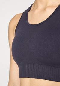 Marineblå crop top med ribbestrikket kant og scoop-hals, laget av glatt, stretchy stoff. Har et sømløst design for komfort og passform.