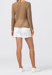 Brązowy sweter dziany z teksturowanym wzorem, długimi rękawami i luźnym krojem, zestawiony z białymi szortami z denimu i białymi trampkami.