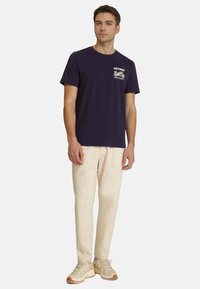 Camiseta de algodón azul marino con un gráfico de motocicleta blanca en el pecho, combinada con pantalones color crema y zapatillas beige.