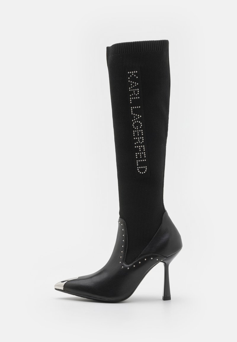 Bottes noires jusqu'aux genoux avec un dessus en maille extensible, talon pointu, talon métallique et accents cloutés. Présente le logo en cristaux sur la tige.