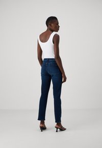 Jean slim bleu avec une texture de tissu lisse, taille haute et design classique à cinq poches, associé à un haut sans manches blanc.