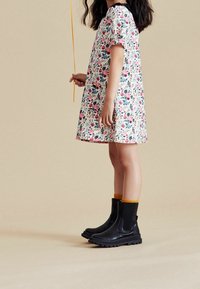 Robe à manches courtes à motifs floraux en blanc, ornée de fleurs roses et bleues. Associée à des bottines noires et des chaussettes à accents jaunes.