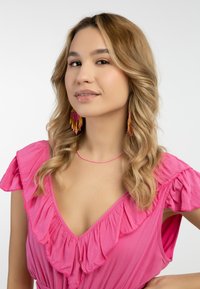 Rózsaszín ruha fodros ujjal, rétegezett anyaggal és mély dekoltázzsal. Gyöngyös rózsaszín és lila fülbevalók egészítik ki a megjelenést. Sima hajtextúra.