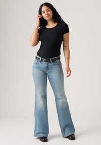 Čierne rebrované tričko s krátkym rukávom v kombinácii so svetlomodrými zvonovými džínsami. Džíny majú vyblednuté detaily a čierny opasok so striebornou prackou.