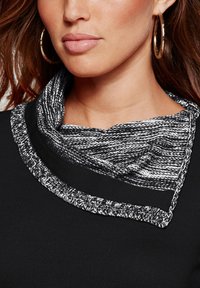 Haut noir avec un col en tricot texturé, présentant un motif tacheté noir et blanc, rehaussé d'une bordure noire lisse.