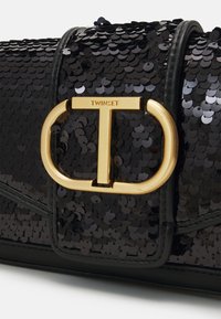 Zwarte paillettenhandtas met een gouden T-vormige sluiting waarop "TWINESET" is gegraveerd, gecombineerd met een gladde zwarte leren basis en accenten.