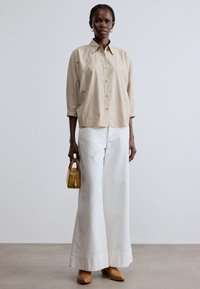 Cămașă bej cu dungi și nasturi, pantaloni albi cu picioare largi, mule bej cu toc și o geantă mică galbenă. Culoare solidă și modele texturate.