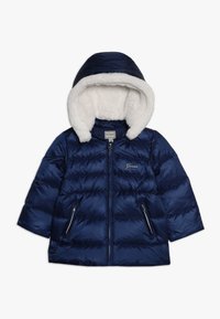 Granatowa kurtka puchowa z białym, futrzanym kapturem, z zamkiem z przodu, zamykanymi kieszeniami oraz logo "Guess" na klatce piersiowej, zaprojektowana na chłodne dni.
