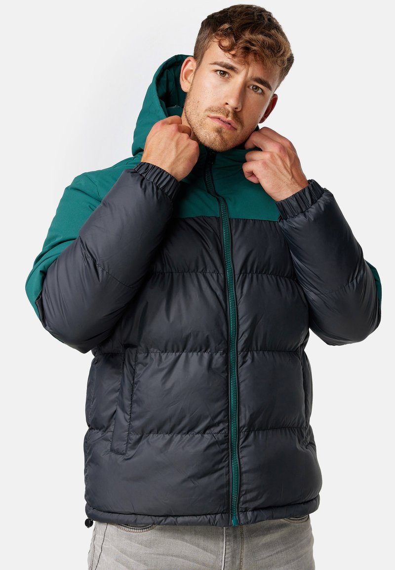 Padded jacket z górną częścią w kolorze szmaragdowym i dolną częścią w kolorze czarnym. Posiada kaptur, zamek błyskawiczny z przodu oraz boczne kieszenie z elastycznymi mankietami.