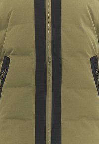 Veste rembourrée verte avec une fermeture éclair devant, présentant des bandes noires sur les côtés et deux poches zippées à l'avant pour plus de fonctionnalité.