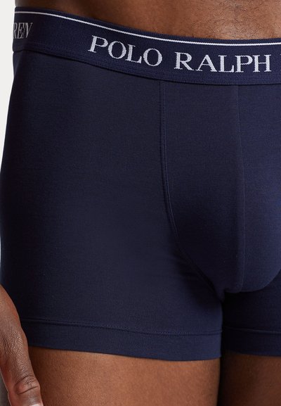 Boxers pour hommes bleu marine avec une ceinture blanche marquée "POLO RALPH" portée sur une peau foncée.