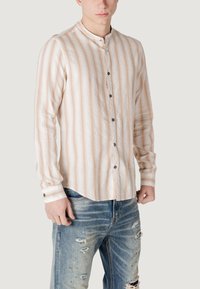 Camicia leggera a maniche lunghe in crema con sottili righe pesche, dotata di colletto a fascia e bottoni scuri a contrasto. Indossata con jeans strappati.